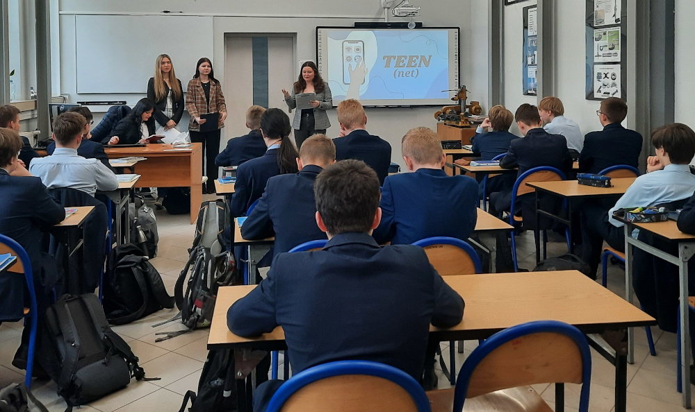 Cztery uczennice z IV LO w Katowicach, które korzystając z tablicy multimedialnej prezentują logo projektu Teen(net). Uczniowie klasy 1G w siedzą w ławkach (ustawionych w trzech rzędach) i z uwagą słuchają