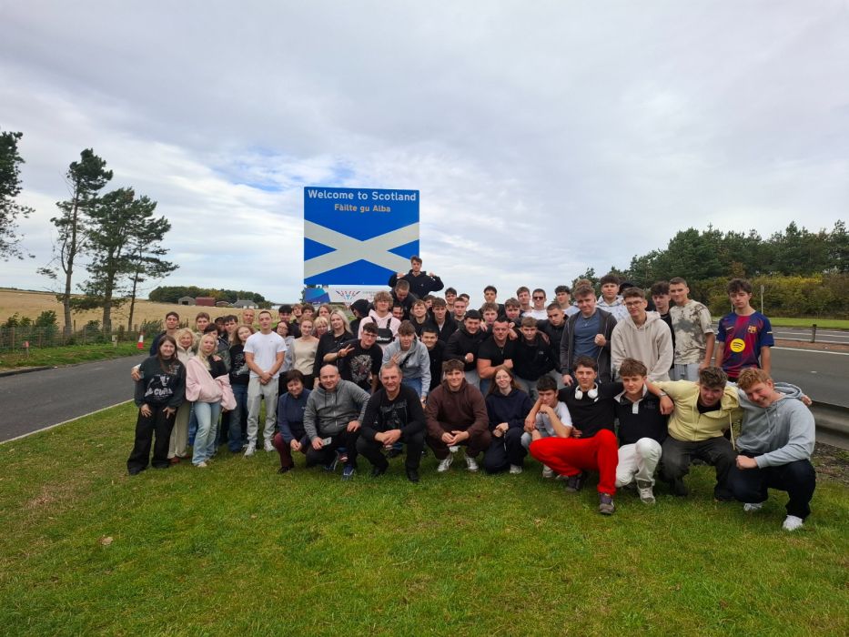 Grupa młodzieży z nauczycielami po tablicą z napisem Welcome to Scotland