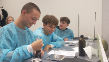 3 uczniów w błękitnych fartuchach ochronnych podczas zajęć praktycznych