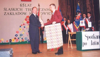 Scena w auli – przywitanie Dyrektora z gościem; w tle dekoracja z napisem 65 LAT ŚLĄSKICH TECHNICZNYCH ZAKŁADÓW NAUKOWYCH