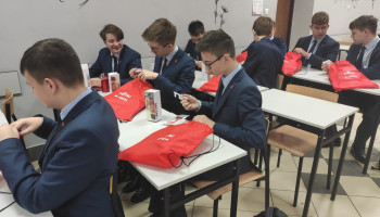 Uczniowie z czerwonymi workami z napisem Fujitsu-P-Tech oglądający otrzymane gadżety