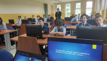 Uczniowie w sali komputerowej podczas zajęć, monitor z prezentacją