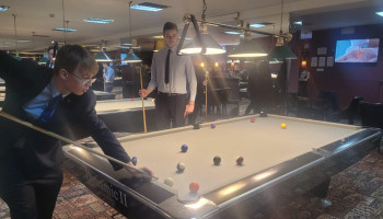 Uczniowie grający w bilard, jeden z uczniów przymierza się do uderzenia w bilę