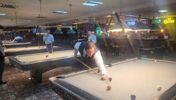 Uczeń grający w bilard, przymierzający się do uderzenia w bilę