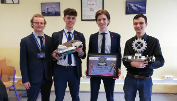 Czterech uczniów prezentujących roboty i dyplom