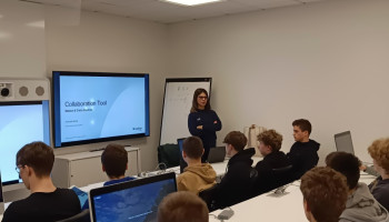 Uczniowie siedzący przy stołach, przed nimi pracownica CISCO prowadząca wykład