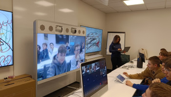 Uczniowie podczas wykładu, przed nimi bardzo duże ekrany, na których widoczne są twarze uczniów