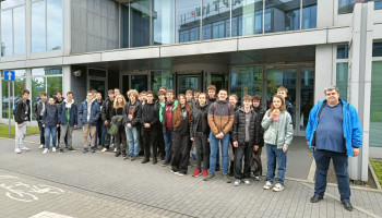 Zdjęcie grupowe uczniów przed nowoczesnym, przeszkolonym budynkiem