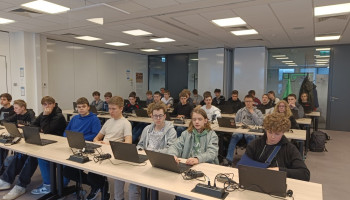 Uczniowie siedzący przy stołach z laptopami