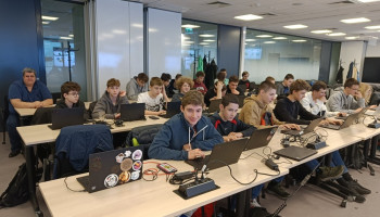 Uczniowie siedzący przy stołach z laptopami