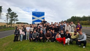 Grupa młodzieży z nauczycielami po tablicą z napisem Welcome to Scotland