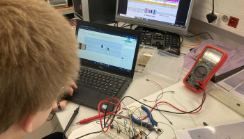 Pracownia montażu układów elektronicznych-1 Materiały dydaktyczne na stanowisku dydaktycznym: komputer, laptop, miernik elektryczny, akcesoria do pomiarów, z boku zwiedzający je ogląda