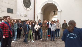 Zwiedzanie – dziedziniec przed kościołem, przewodnik opowiada uczestnikom pielgrzymki stojącym w grupie