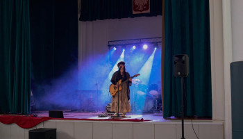 Występ - wokalistka na scenie z gitarą, ubrana w strój artystyczny vintage