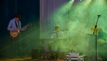 Występ - gitarzysta z lewej, na środku sceny akompaniujący na keyboardzie, oświetlenie zadymiona zieleń