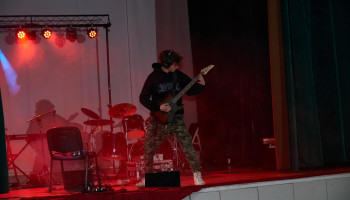 Występ - solowy występ rockowy gitarzysty, ekspresyjny, w tle perkusja, tło czerwone