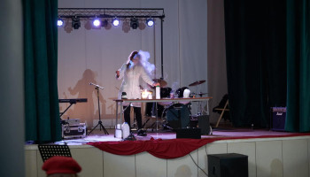 Występ - na scenie pokaz chemiczny uczennicy w białym fartuchu ochronnym z klasy analiza chemiczna, na stoliku akcesoria do pokazu