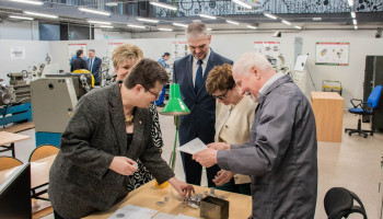 pani minister i pani poseł podziwiają figury szachowe, wytoczone na warsztatach; kierownik warsztatów i nauczyciel zawodu