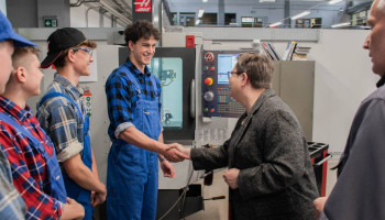 pani minister wita się z uczniem w ubraniu roboczym, w tle obrabiarka CNC