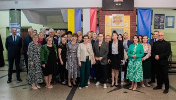 pamiątkowe zdjęcie gości i grona pedagogicznego (pozycja stojąca) w holu szkoły przed tablicą z napisem: 90 lat Śl.TZN i tarczą „Złote Technikum”