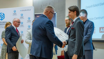Uroczystość wręczenia nagród Olimpiady Wiedzy Elektroników i Mechatroników ELEKTROMECHATRON. Politechnika Bydgoska 14.06.2024. Po prawej stronie Laureat ze Śl.TZN w Katowicach, Maksymilian Zych przyjmuje gratulacje od organizatorów oraz bon wartościowy stanowiący nagrodę za uzyskanie III miejsca w Olimpiadzie.