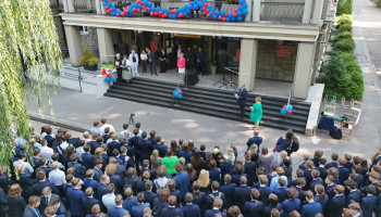 przed odsłonięciem Beboka (na podmurówce przykryty czerwoną narzutką); goście, gospodarze, nauczyciele, uczniowie w garniturach (u dołu zdjęcia zwróceni w stronę wejścia do szkoły, widoczni tyłem)