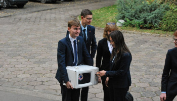 uczeń z mikrofalówką, obok 2 zainteresowane uczennice i 1 uczeń