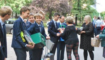 grupa uczniów z gadżetami-plecakami, pani dyrektor wręcza jednemu nagrodę