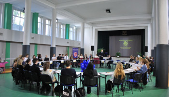 Rozpoczęcie forum: powitanie przewodniczącego SU Śl.TZN, uczestnicy na miejscach przy stolikach ustawionych w „okrągły stół” w auli szkolnej, w środku okręgu dekoracja (kształt kwiatu/piramidy) z niebieskich balonów z logo szkoły 