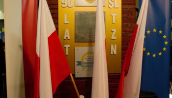 flagi państwowe przed tablicą pamiątkową w holu szkoły
