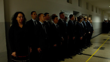 nauczyciel oraz jedna z klas przed salą wykonują hymn